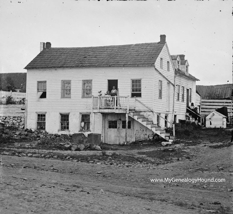 John L. Burns at his home in Gettysburg, Pennsylvania, seated on the second floor porch with his crutches and musket rifle.